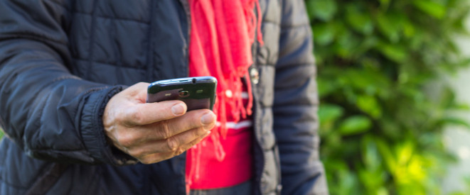 Datenautomatik beim Handytarif: Das ist zu beachten. Eine Person mit rotem Schal und dunkler Daunenjacke hält ein Smartphone in der Hand.