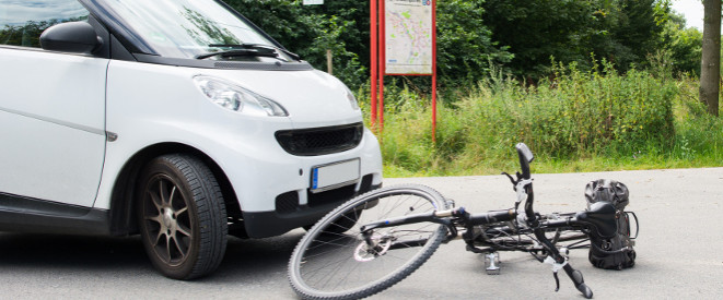 Fahrradunfall: Unachtsamer Radfahrer trägt Alleinschuld. Neben einem weißen Smart liegt ein Rad auf dem Asphalt.