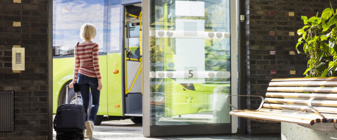Gepäckverlust im Fernbus: Recht auf Entschädigung. Eine junge Frau geht aus der Tür eines Terminals, vor der ein Reisebus steht.