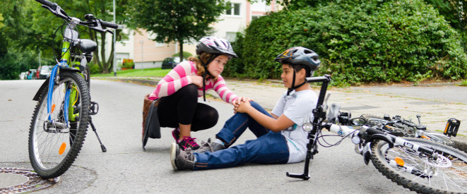 Gesetzliche Unfallversicherung für Schüler: Wann greift sie? Ein Junge mit Fahrradhelm sitzt auf dem Boden und hält sich das Knie. Daneben liegt ein umgestürztes Rad. Ein Mädchen mit Fahrradhelmhockt neben ihm und tröstet ihn. 