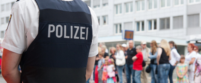 Mindestgröße bei Polizei und Co.: Diese Regelungen gibt es. Ein Mann mit Polizei-Schutzweste steht vor einer kleinen Menschentraube.