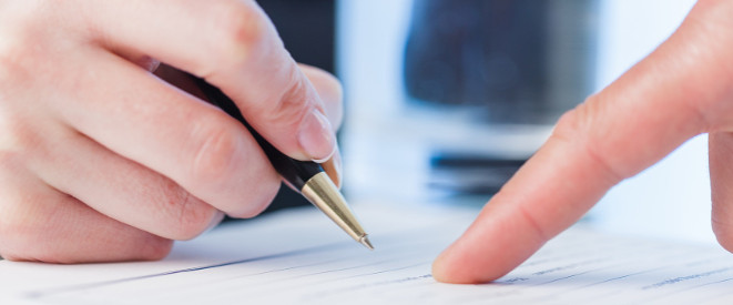 Verfahrenskostenhilfe auch bei Wohneigentum möglich. Ein Finger deutet auf ein Dokument; daneben liegt eine Hand, die einen Kugelschreiber hält.