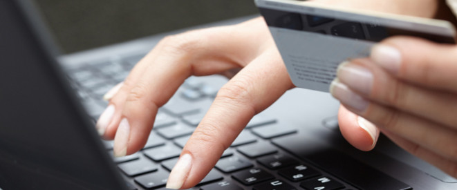Fake-Shops: Schutz vor Betrug mit Thermomix und Co. Ein Frau hält eine Geldkarte in der einen Hand und tippt mit der anderen Hand auf einem schwarzen Laptop.