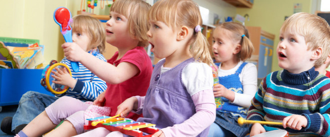 Kein Kita-Platz: Stadt muss Mehrkosten erstatten. Mehrere Kleinkinder sitzen auf dem Boden, halten Musikinstrumente in den Händen und schauen in eine Richtung.