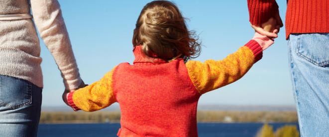 Urteil: Kinder können Vaterschaftstest nicht erzwingen. Vor einem See halten Mutter und Vater die Hände ihres Kindes.