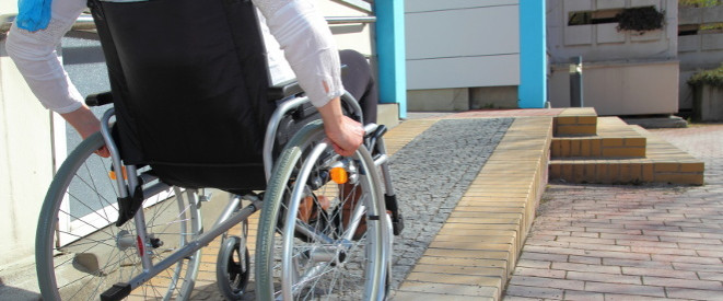 Volle Erwerbsminderungsrente: Wann wird sie gezahlt? Ein Rollstuhlfahrer fährt neben einer Treppe eine Rollstuhlrampe hinauf.
