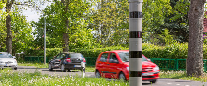 Fahrverbot und Führerscheinentzug: Die Rechtslage. Auf einer Straßen fahren Autos, davor steht ein Blitzer.