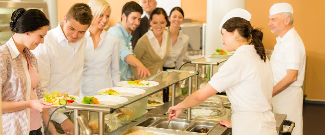 Gesetzlicher Mindestlohn: Sonderzahlungen sind anrechenbar. Junge Menschen stehen in der Schlage einer Kantine. Eine Frau und ein Mann geben das Essen aus.