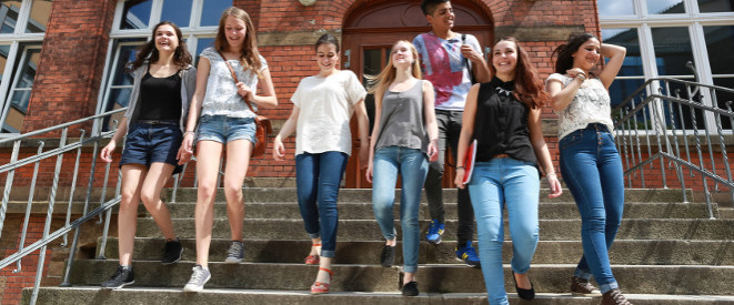 Hitzefrei in der Schule: So unterschiedlich ist es geregelt. Jugendliche gehen eine Steintreppe vor einem roten Backsteingebäude hinab.