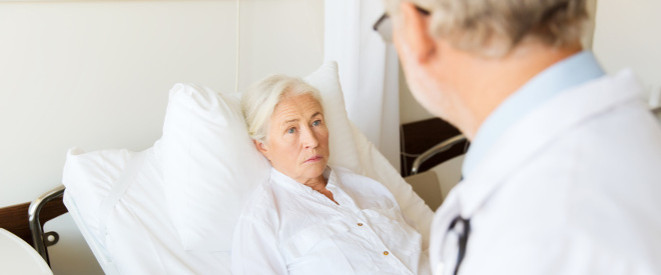 Nottestament: Diese Regelungen gelten. EIne ältere Frau mit weißen Haaren liegt in einem Krankenhausbett. Vor ihr steht ein Arzt.