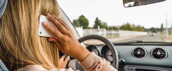 Telefonieren am Steuer: Urteil zeigt Gesetzeslücke auf. Eine Frau mit blonden Haaren sitzt am Steuer eines Autos und hält sich ein Handy ans Ohr.