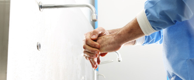 Wo ist Händehygiene Pflicht? Richtlinien und Rechtslage. Eine Person in blauem Kittel wäscht sich die Hände unter einem Wasserhand.