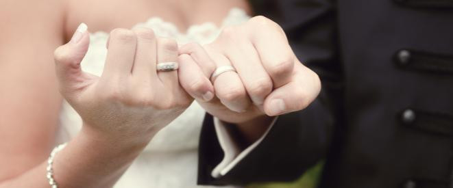 Behördengänge nach der Hochzeit: die Checkliste. Ein Brautpaar das seine kleinen Finger der rechten Hand verschlungen hält.