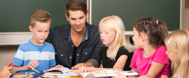 Bildungspaket: Nachhilfe für bedürftige Kinder möglich. Ein junger Lehrer sitzt mit jungen Schülern vor mehreren Büchern.