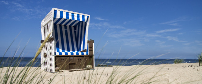 Erholungskur: Keine Entgeltfortzahlung für Arbeitnehmer. EIn blau-weiß gestreifter Strandkorb steht in den Dünen, dahinter sieht man das Meer.