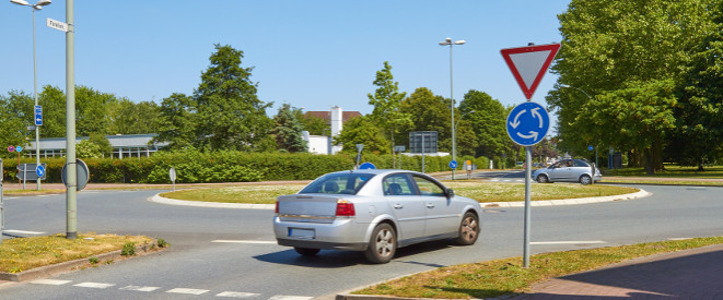 Vorfahrt im Kreisverkehr: Die Rechtslage. Ein silbernes Auto biegt in einen Kreisverkehr ein.