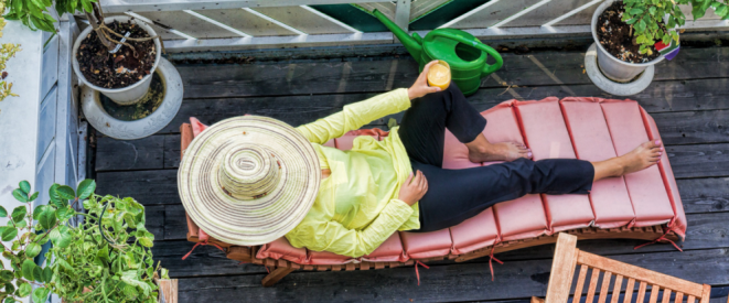 Eigene Wohnung als Ferienwohnung vermieten: Erlaubt? Ein Frau mit Sonnenhut liegt auf einer bepflanzten Terrasse.