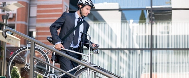 Dienstfahrrad statt Dienstwagen: Ihre Rechte als Arbeitnehmer. Ein Mann im Anzug und Fahrradhelm trägt ein Herrenrad eine kleine Treppe herunter.