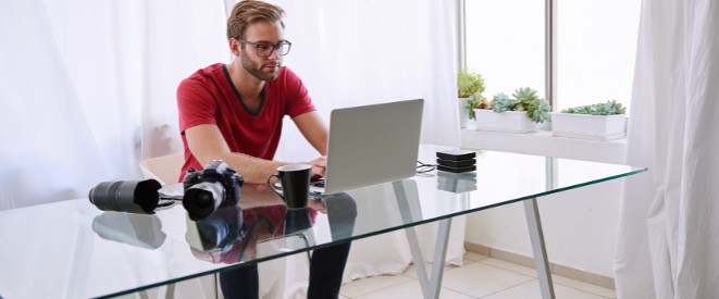 Domain anmelden: Namensschutz und Namensrecht beachten. Ein Mann mit Brille sitzt an einem gläsernen Schreibtisch an einem Laptop.