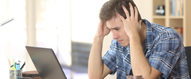 Online Anzeige erstatten: Tipps für die Anzeige im Netz. Ein junger Mann sitzt vor einem Notebook und vergräbt die Hände in den Haaren. 