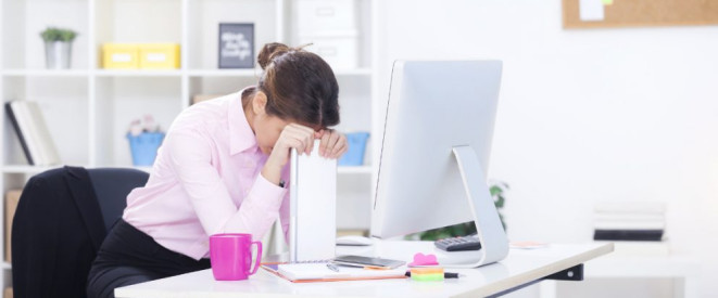 Straining: Mobbing durch Langeweile im Büro. Eine Frau sitzt im Büro und stützt Ihren Kopf auf einen Aktenordner. Das Gesicht ist verdeckt.