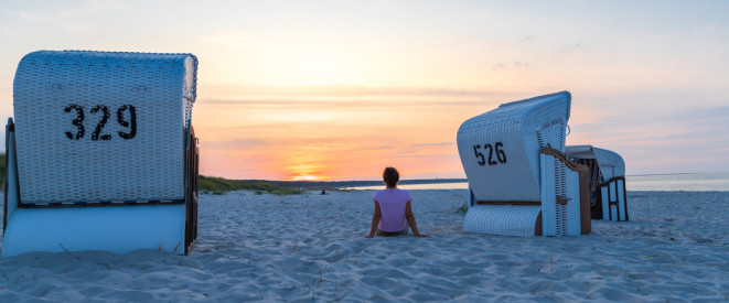 Frau sitzt im Sonnenuntergang zwischen zwei Strandkörben 