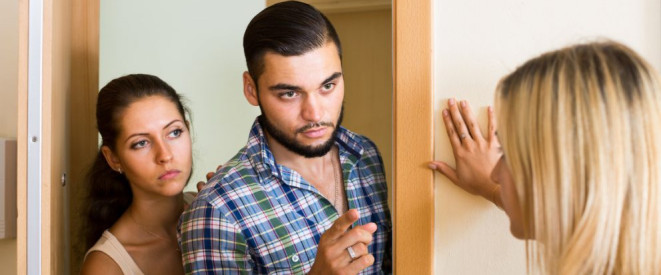 Hausverbot erteilen: Das erlaubt das Hausrecht. Ein junges Paar steht in der Wohnungstür einer anderen Frau gegenüber. Der Mann hebt seinen Finger.