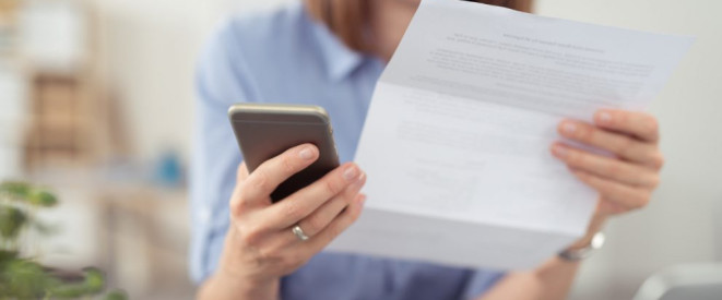 Lohnnachzahlung: Verjährungsfrist unwirksam ohne Mindestlohn. Eine Frau hält ein Formular in der einen und ein Smartphone in der anderen Hand.