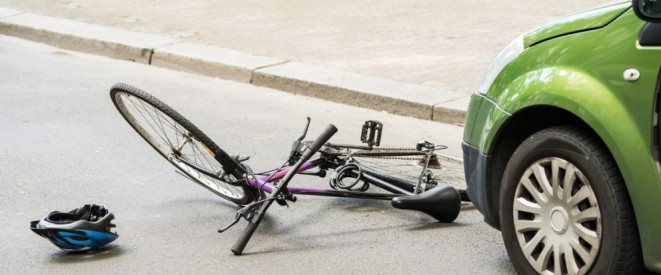 Radweg falsch benutzt: Radfahrer hat Mitschuld an Unfall. Vor einem grünen Auto liegen ein umgestürztes Fahrrad und ein Fahrradhelm.