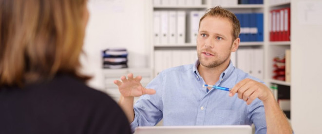 Betriebsrente: Was passiert bei einem Jobwechsel? Ein Mann in blauem Hemd gestikuliert mit einen Händen vor einem Notebook. Er sitzt einer Frau in schwarzem Blazer gegenüber.