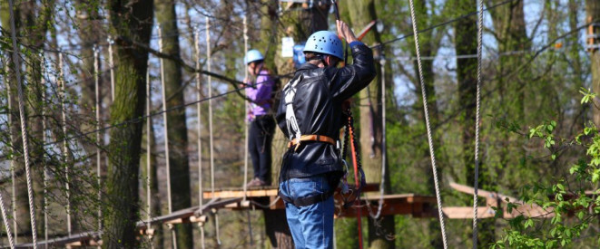 Urteil: Schmerzensgeld nach Unfall im Kletterpark. Zwei Menschen mit Helm klettern in einem Hochseilgarten.