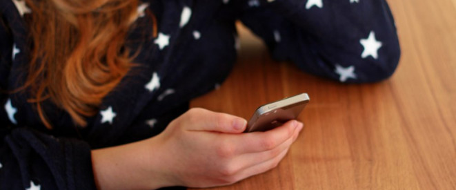 WhatsApp-Datenschutz: Weitergabe an Facebook rechtens? Ein Mädchen mit roten Haaren und schwarzem Pullover mit weißen Sternen hält ein Smartphone in der Hand.