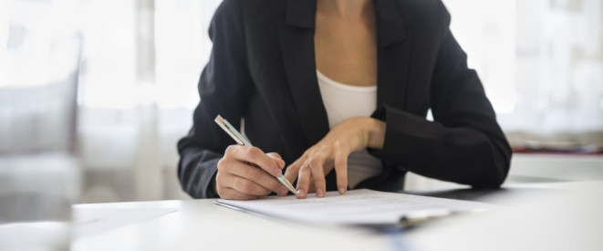 Arbeitszeiterhöhung: Befristung und weitere Bedingungen. Eine Frau im Blazer schreibt mit einem Stift auf einem Blatt Papier.