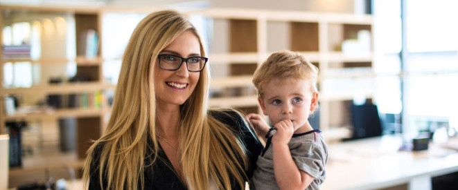 Elternzeit verkürzen: Ihre Rechte als Arbeitnehmer. Ein Frau mit langen blonden Haaren und Brille trägt einen kleinen Jungen auf dem Arm.