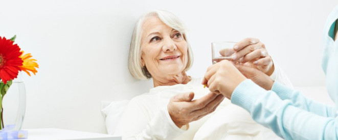 Medizinische Zwangsbehandlung: Die Rechtslage. Eine ältere Frau liegt im Bett. Ihr werden ein Glas Wasser und Tabletten gereicht.