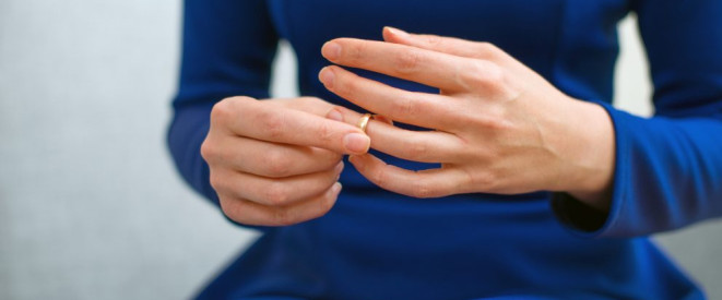 Trennungsjahr vor der Scheidung: So läuft es ab. Eine Frau in blauem Kleid zieht einen goldenen Ring über den Ringfinger.