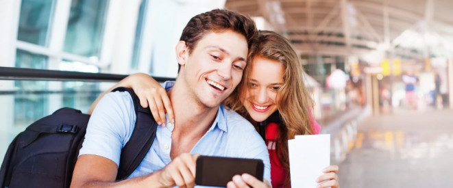 Fernreisen: Tipps zu Reisepass, Visum und Co. Ein junger Mann und eine junge Frau gucken in einem Flughafen-Terminal gemeinsam auf ein Smartphone.