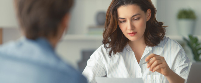 Zwischenzeugnis anfordern: Haben Arbeitnehmer Anspruch darauf? Eine junge Frau mit kurzen Haaren sitzt an einem Büro-Schreibtisch einer älteren Frau gegenüber.