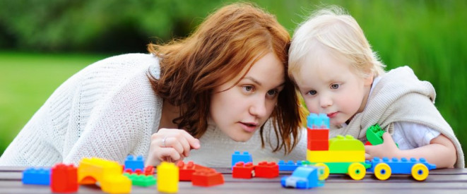 Au-pair aufnehmen: Was die Gastfamilie wissen sollte. Eine junge Frau schaut gemeinsam mit einem Kleinkind auf eine Plastik-Eisenbahn.