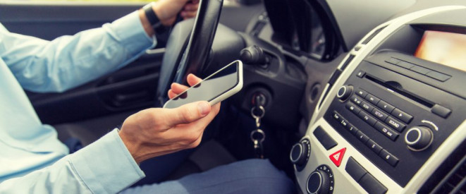 Unfall mit dem Firmenwagen: Wie ist die Haftung geregelt? Ein Mann sitzt hinter dem Steuer eines Autos und hält ein Smartphone in der Hand.