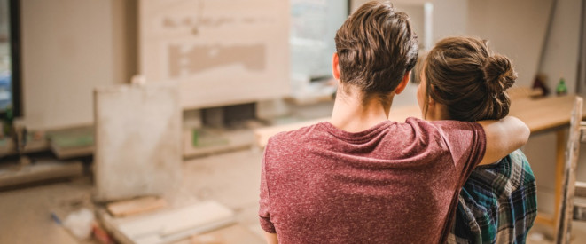 Junges Paar steht in neuer Wohnung auf Baustelle und schaut sie sich an