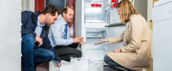 Küchenausstattung: Darauf haben Mieter Anspruch. Eine Frau und zwei Männer hocken vor einem leeren Kühlschrank und begutachten seine Ausstattung.