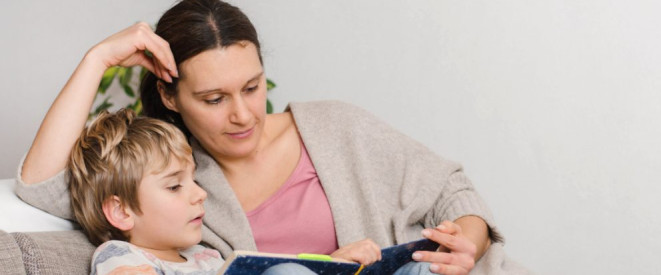 Unterhaltsvorschuss: Wer hat Anspruch darauf? Eine Mutter sitzt mit ihrem Sohn auf einer Couch und liest ein Buch.
