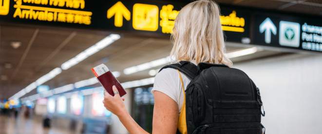 Frau mit Reisepass und Ticket in der Hand unter digitaler Anzeige am Flughafen