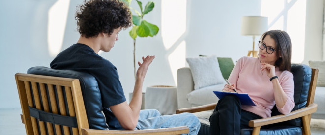 Psychotherapeutin und Patientin sitzen sich auf Stühlen gegenüber bei Therapiestunde