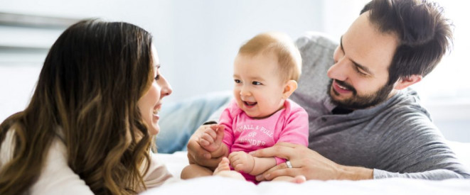 Paar liegt mit einem lachenden Baby auf einem Bett