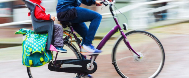 Eine Person auf dem Fahrrad mit Kind im Kindersitz auf dem Gepäckträger