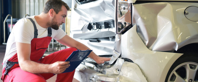 Mann KFZ-Mechaniker in rotem Overall prüft in Werkstatt Schaden an Auto