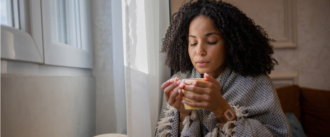 Frau sitzt vor Fenster mit Tasse in der Hand