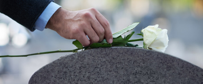 Hand legt weiße Rose auf Grabstein